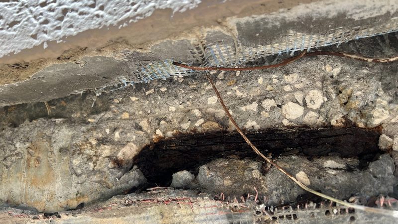 Close-up of concrete spalling and corroded reinforcing steel documented during a CSI building evaluation