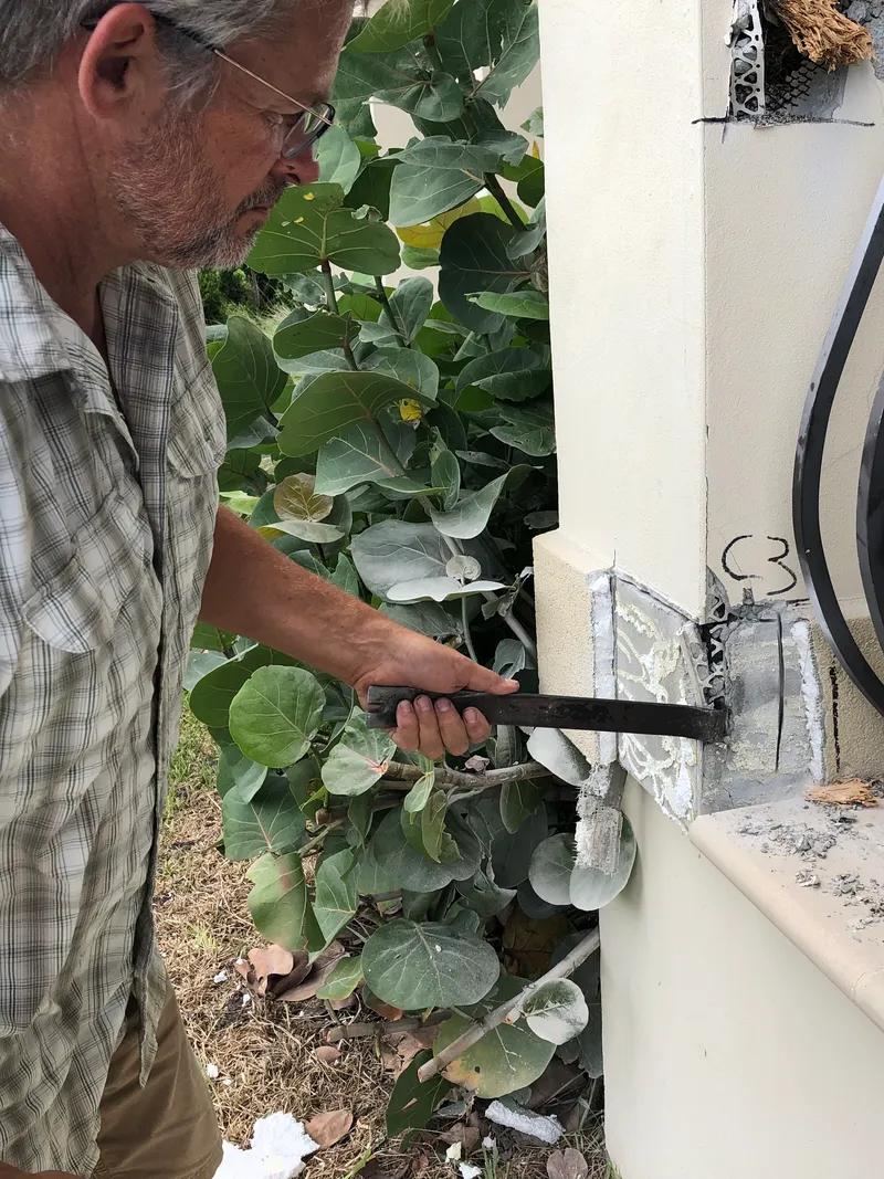 A field worker uses a pry bar at an opening in an exterior wall.