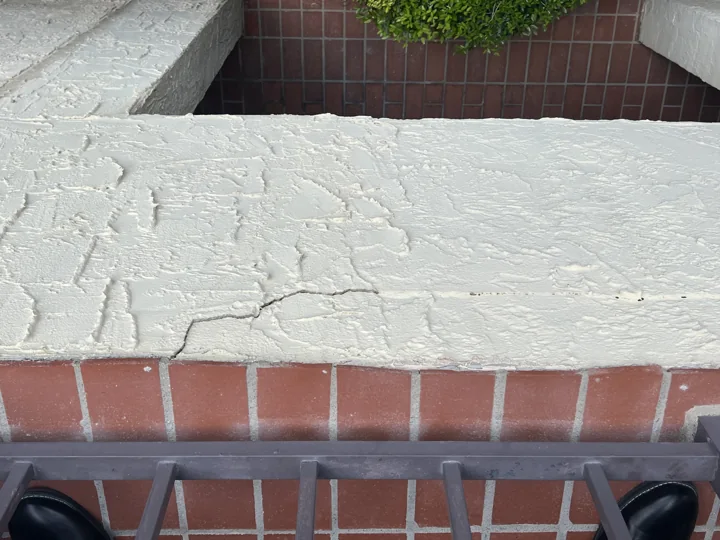Existing cracking and irregular finishes along a tiled walkway ledge.