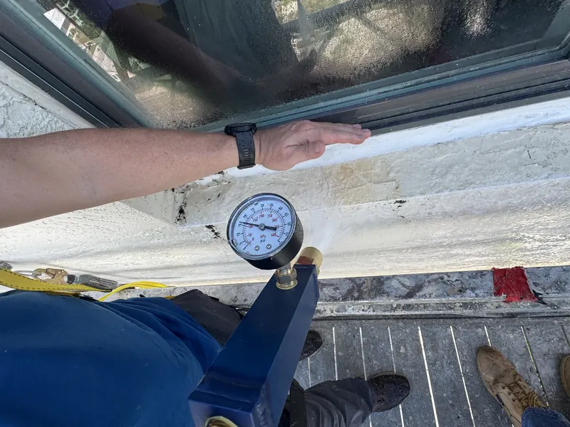 Spray nozzle with a pressure gauge held at a high-rise window sill during a water test from a swing stage