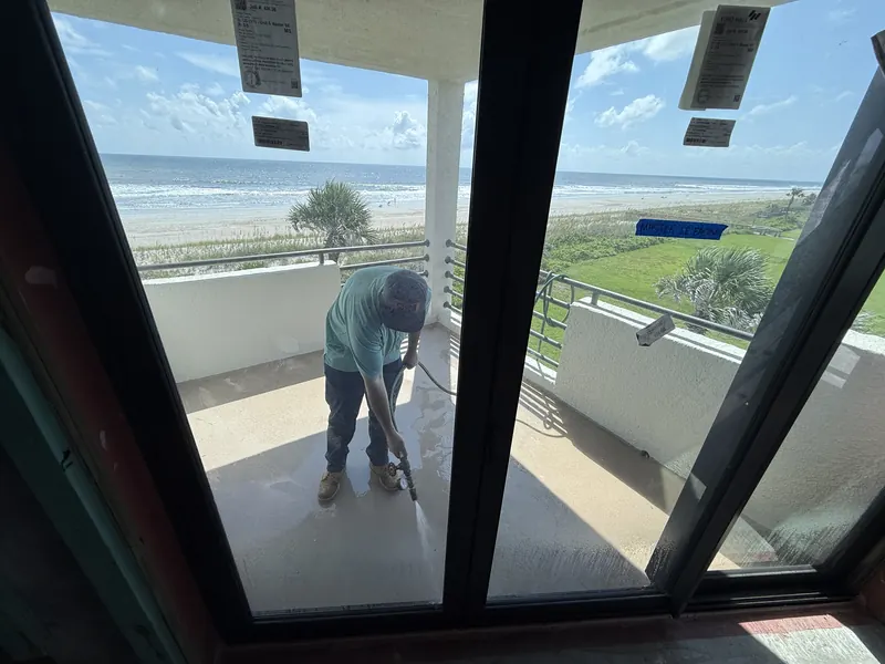 Technician spraying water at a newly installed oceanfront sliding glass door, viewed from inside the unit
