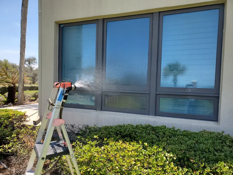Technician on a ladder spraying water from a calibrated nozzle at a row of first-floor condominium windows