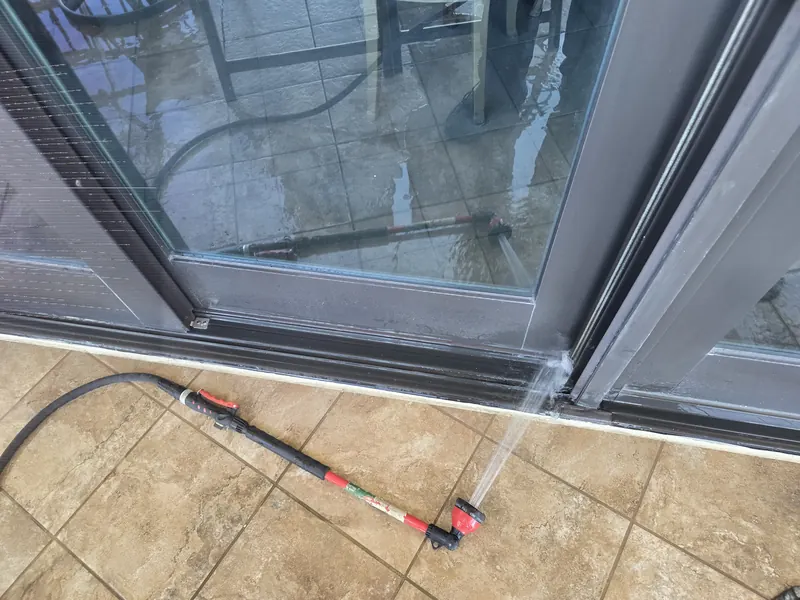 Spray wand directing water at the threshold of a sliding glass door on a tiled balcony